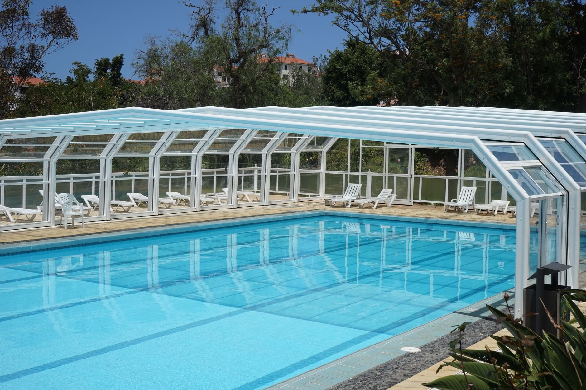 A serene outdoor poolside scene featuring a modern cover and surrounded by lush greenery.