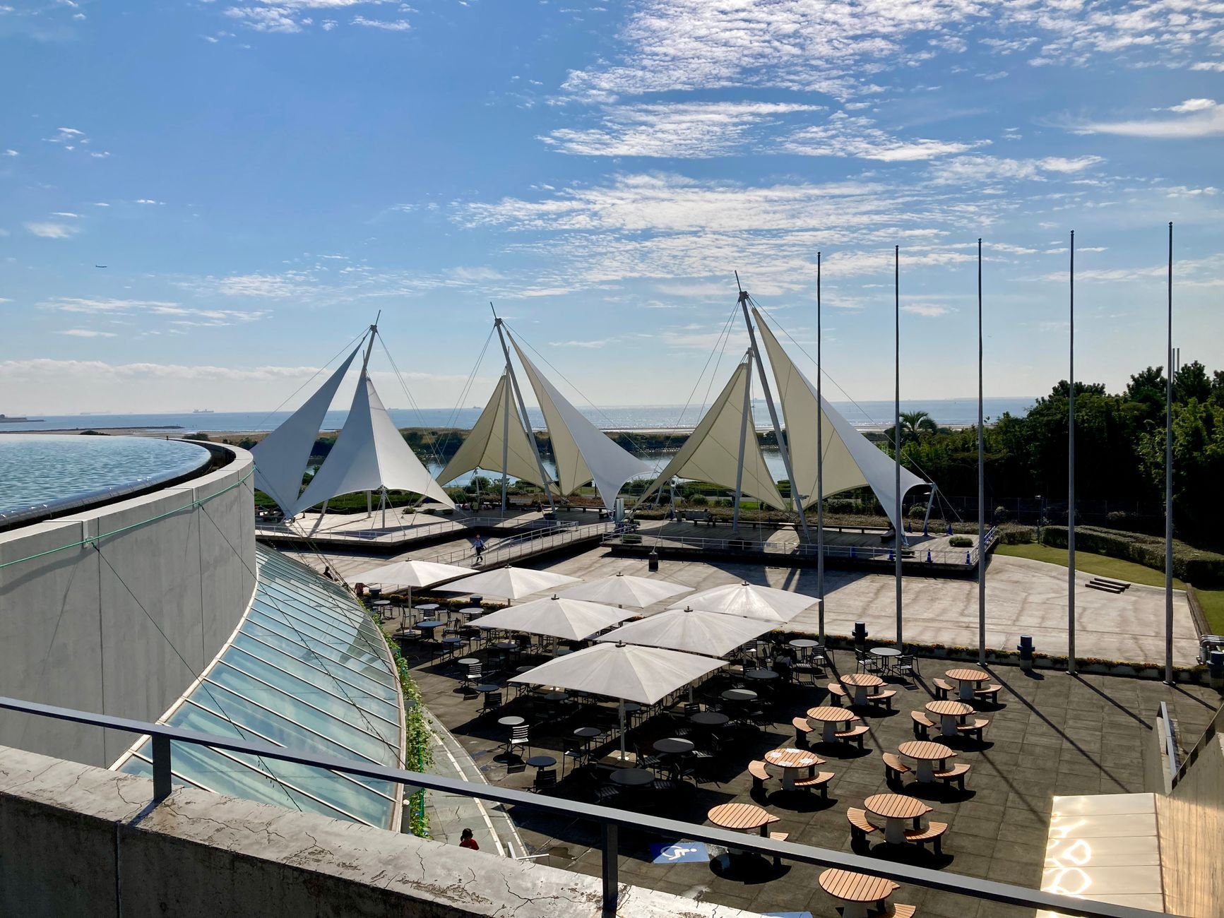 Stunning view of a modern terrace with sail-like structures and shaded seating under a clear blue sky.
